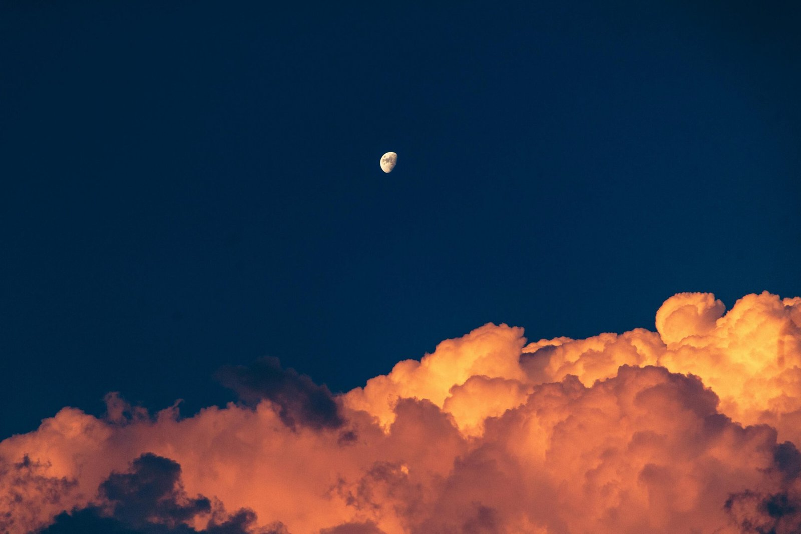 Capture of the moon rising over dramatic red clouds during a vibrant sunset.