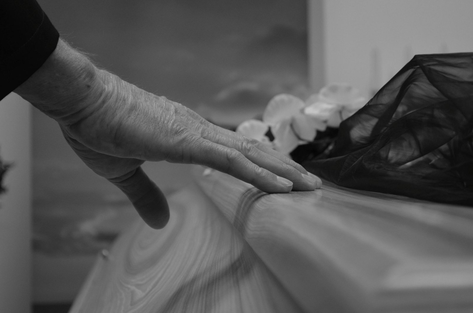 A touching black and white image of a hand resting on a coffin, symbolizing a final farewell.